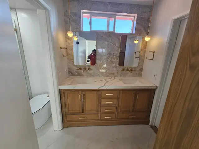 Bathroom with a wood double vanity, stone slab backsplash, two framed mirrors and brass wall sconces