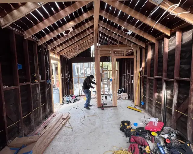 ADU under construction with exposed wood framing and roof rafters as a crew member works inside