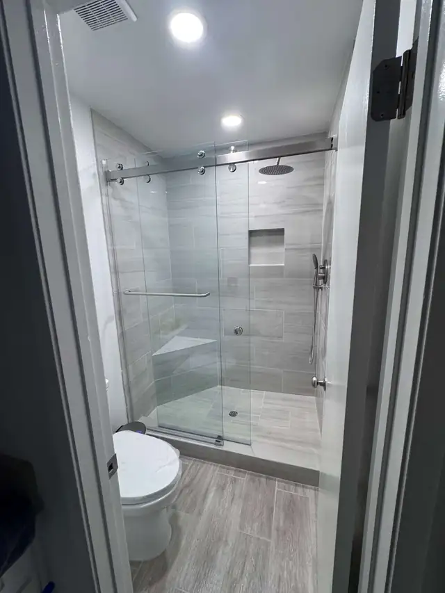 Reseda bathroom remodel with a sliding glass shower door, gray wall tile, a built-in niche and wood-look floor tile
