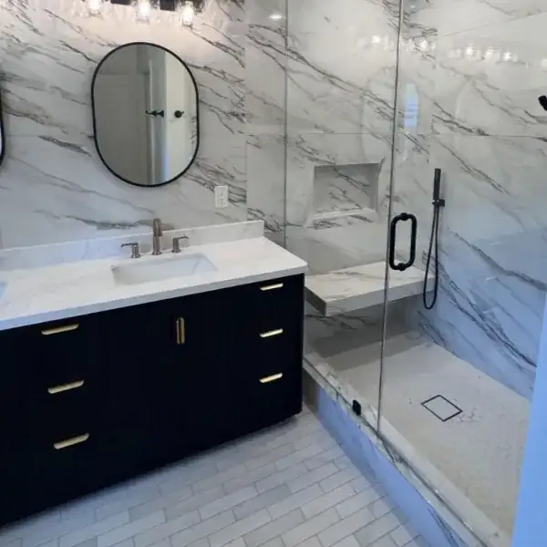 Thousand Oaks bathroom with marble-look tile, a frameless glass shower with a bench and a black vanity with brass pulls