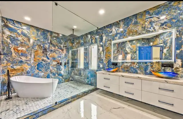 Calabasas primary bath with blue and gold stone slab walls, a freestanding tub, a lit mirror and a long white vanity