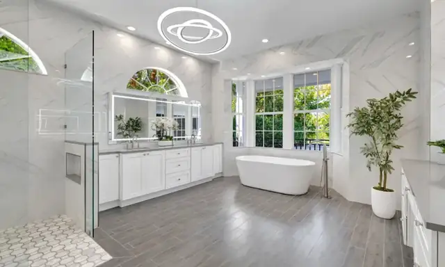 Santa Clarita primary bath with marble-look wall tile, a glass shower, a freestanding tub and a double vanity under arched windows