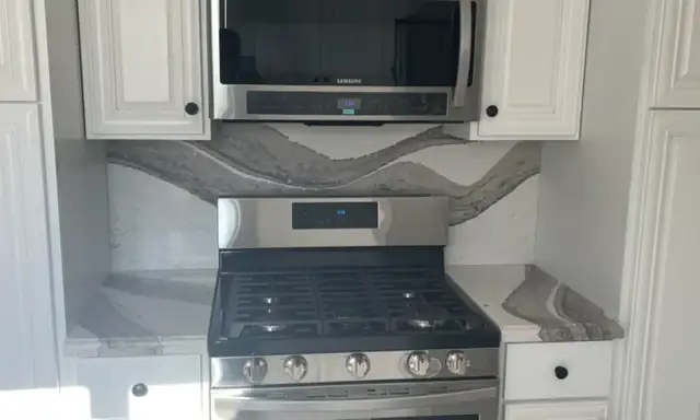 Kitchen with white cabinets, a stainless gas range and a stone slab backsplash with wavy gray veining