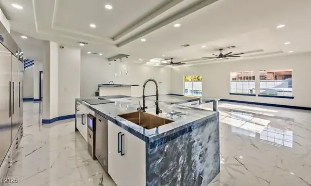Open kitchen with a blue granite island, a copper sink, white cabinets and polished marble-look floor tile