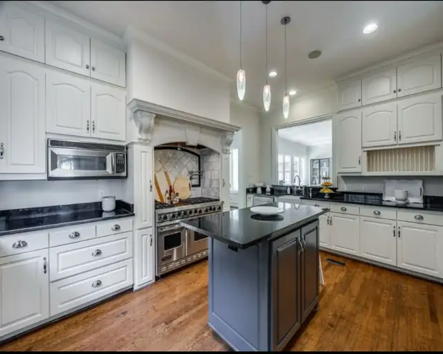 Santa Clarita kitchen with white cabinets, a dark island with a black countertop, pendant lights and wood floors