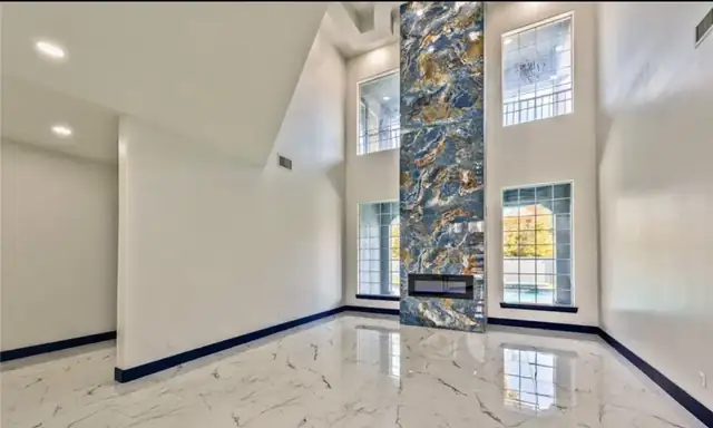 Two-story living room remodel with polished marble-look floor tile and a full-height decorative stone fireplace wall