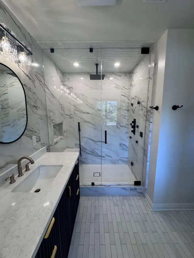 Santa Clarita bathroom with a frameless glass walk-in shower, marble-look wall tile and a navy vanity with brass faucet