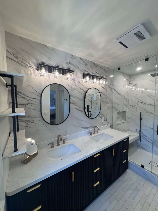 Remodeled Santa Clarita bathroom with a navy double vanity, two oval mirrors, marble-look tile walls and a glass shower